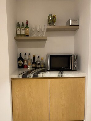 Eine Küche mit einer Mikrowelle, Weinflaschen und Gläsern auf Regalen.