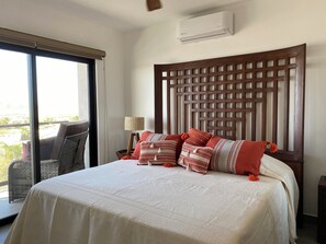 Une chambre d’hôtel avec un grand lit, une tête de lit en bois, une fenêtre donnant sur un beau paysage et un appareil de climatisation.