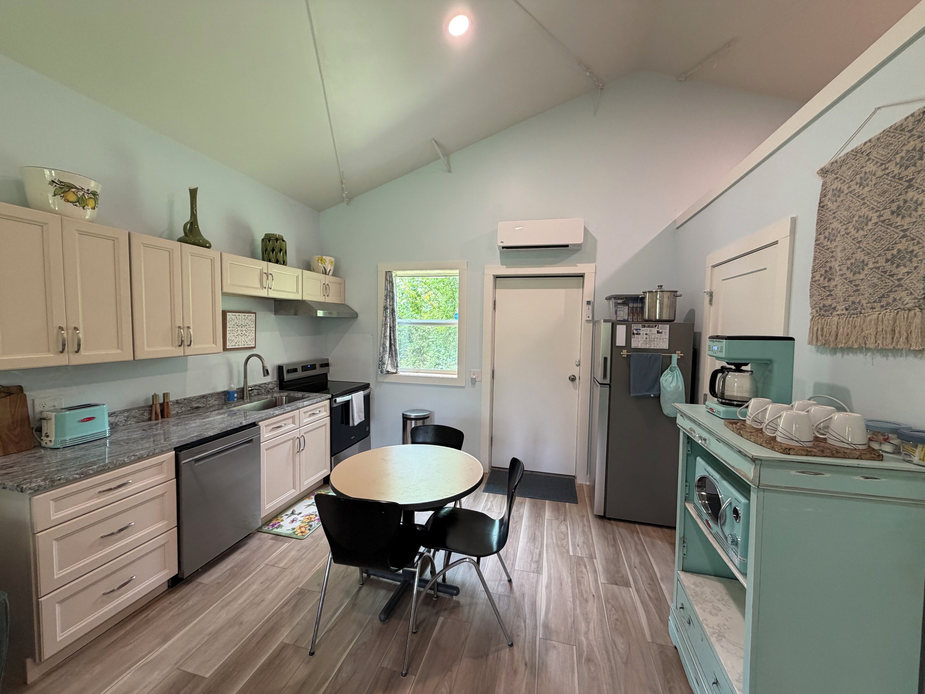 A kitchen with a dining table, chairs, cabinets, a refrigerator, a coffee maker, and a window.
