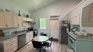 A kitchen with a dining table, chairs, cabinets, a refrigerator, a coffee maker, and a window.