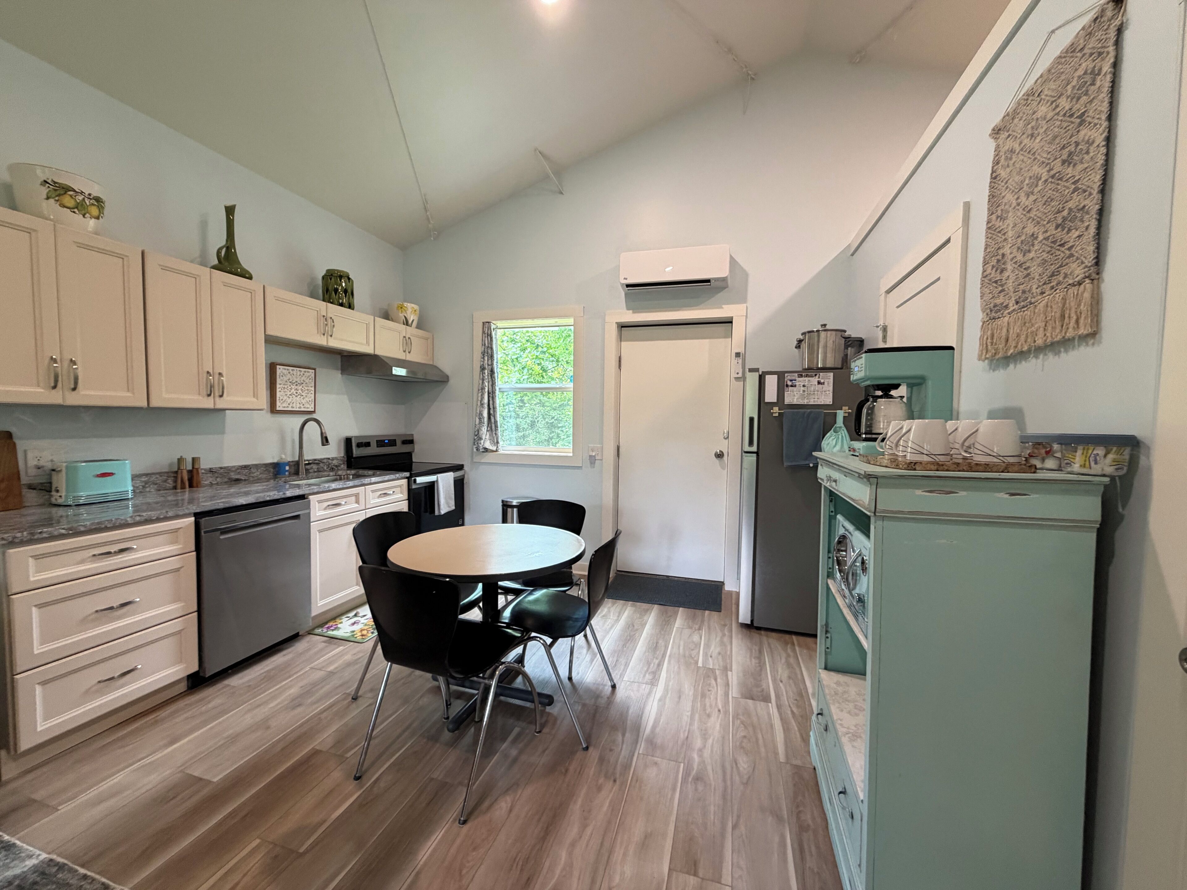 A modern kitchen with white cabinets, a dining table with chairs, a refrigerator, and a coffee machine.