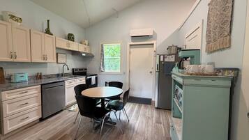 A modern kitchen with white cabinets, a dining table with chairs, a refrigerator, and a coffee machine.
