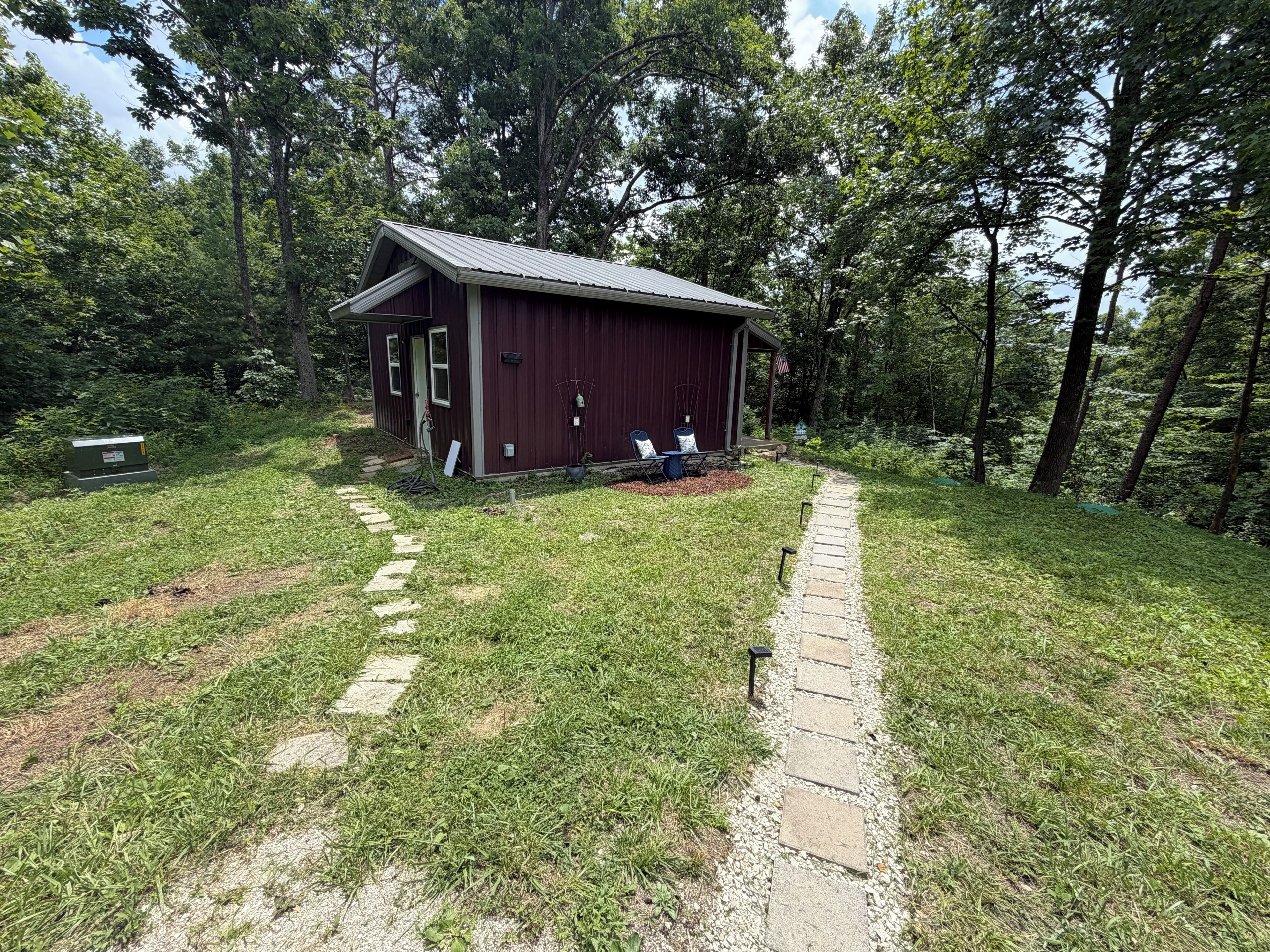 En liten, envåningsbyggnad med en röd fasad, en veranda med två stolar och en asfalterad gångväg som leder fram till den.