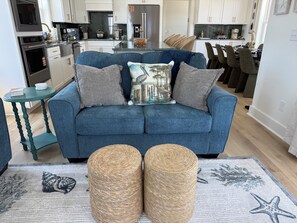 A living room with a blue sofa, two poufs, a small table, and a rug with a starfish design. - New Luxury Beach Retreat  4 Bedrooms 3 King beds  Elevator  Steps to the Beach (Carolina Beach)