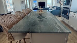 Una cocina moderna con una isla central, electrodomésticos integrados y un comedor con sillas de mimbre.