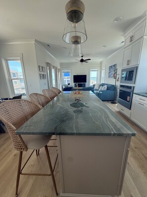 A modern kitchen with a central island, built-in appliances, and a dining area with wicker chairs. - New Luxury Beach Retreat  4 Bedrooms 3 King beds  Elevator  Steps to the Beach (Carolina Beach)