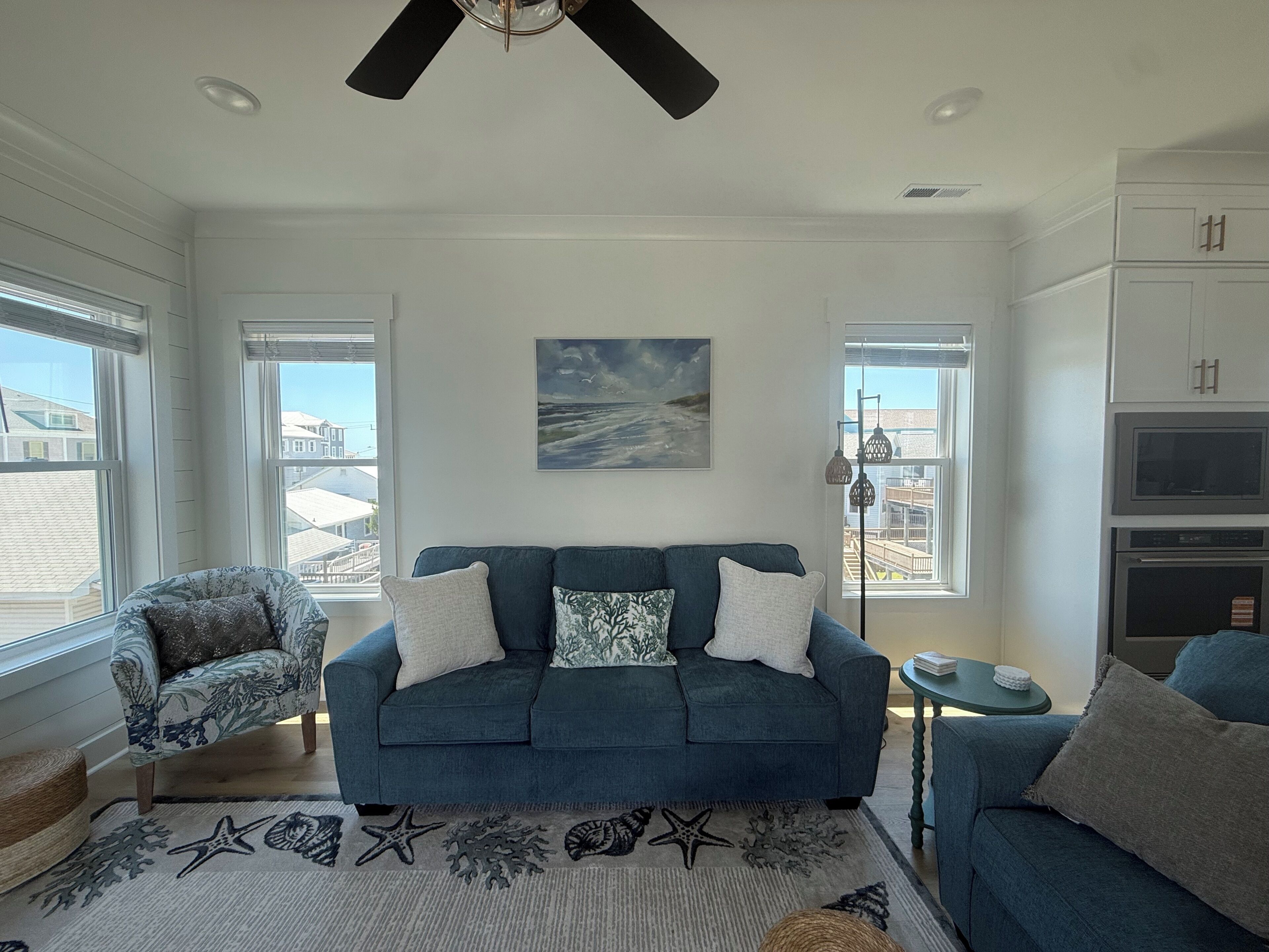 A living room with a blue sofa, a patterned armchair, a starfish rug, and a painting of a seascape.