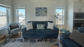 Una sala de estar con un sofá azul, un sillón estampado, un tapete con forma de estrella de mar y un cuadro de un paisaje marino.