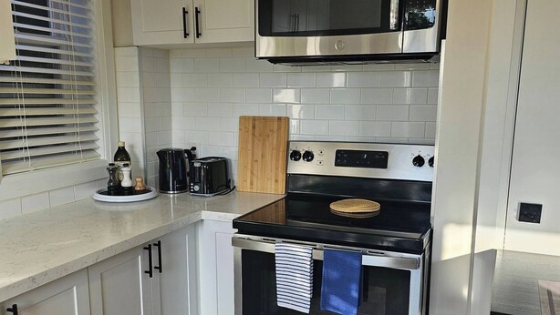 Una cocina con armarios blancos, horno de acero inoxidable, microondas y tostadora.