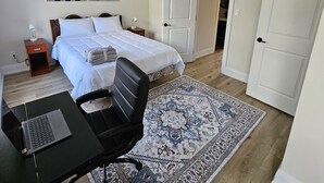 Un dormitorio con cama, escritorio con computadora portátil, silla, alfombra estampada y dos puertas.