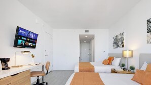 A hotel room with a desk, two beds, a TV, and artwork on the walls. - 28th Floor Studio w Marina View & Pool (Hallandale Beach)