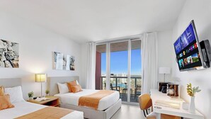 Hotellihuone, jossa on kaksi sänkyä, työpöytä, televisio ja parveke, jolta on näkymä kaupunkiin.