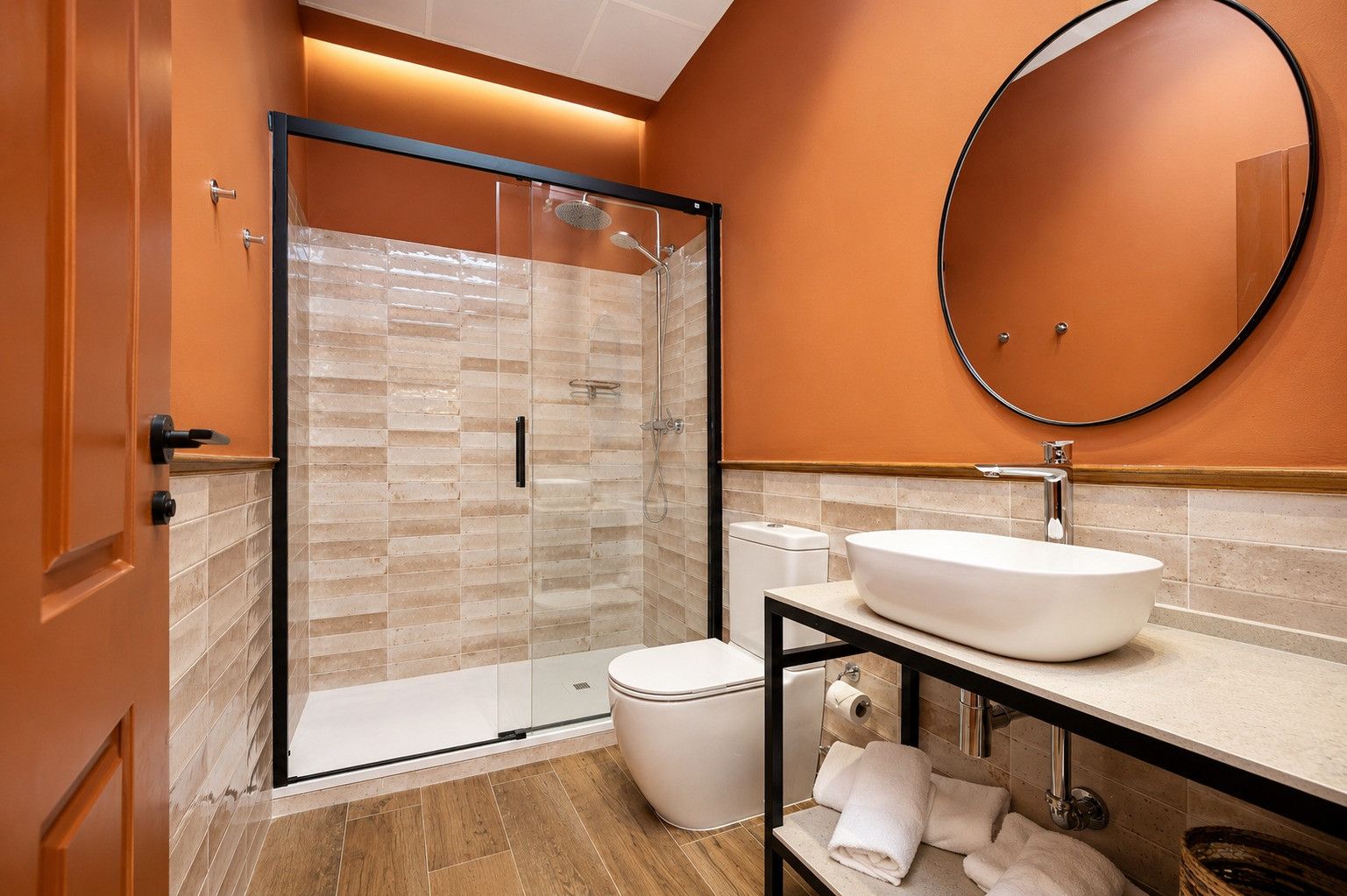 Un baño moderno con ducha de vidrio, lavamanos blanco y espejo redondo.