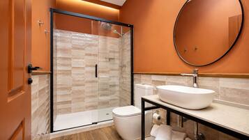 Un baño moderno con ducha de vidrio, lavamanos blanco y espejo redondo.