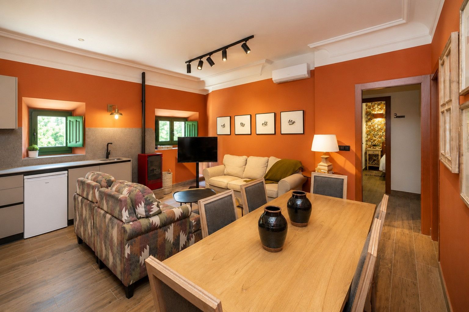 Un espacio habitable compacto con kitchenette, sofá, televisión y mesa de comedor.