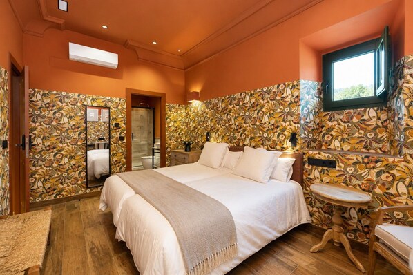 A bedroom with a large bed, a bedside table, a mirror, a window, and a bathroom with a toilet and sink.