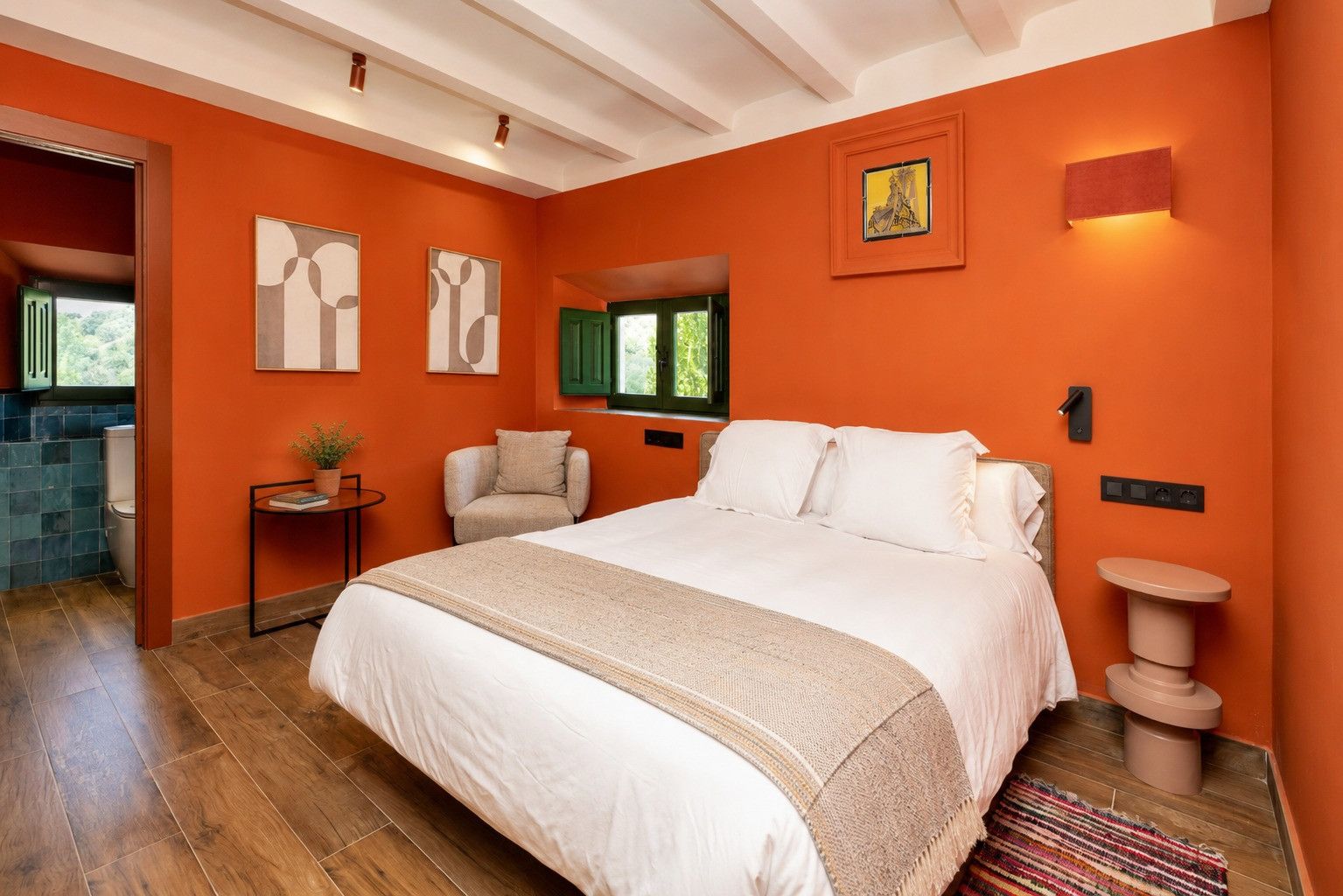 Un dormitorio con una cama grande, una silla, una mesita y un ventanal.