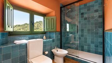 Un baño con inodoro, bidé y zona de ducha, con azulejos azules y vistas a través de una ventana.