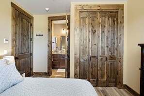 A bedroom with a bed, wooden doors, and a bathroom visible through an open door. - Beautiful 2-bedroom apartment in Sutherlin - Minutes from I-5! (Sutherlin)