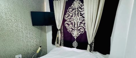 Un dormitorio con una cama, un televisor montado en la pared y un enchufe.