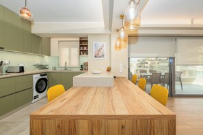A modern kitchen with a wooden dining table, yellow chairs, a washing machine, and a large window.
