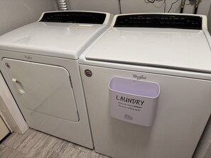 Two white Whirlpool washers in a laundry room with a door and a label on the right one. - Spacious 6-bedroom house in quaint Graham with AC (Graham)