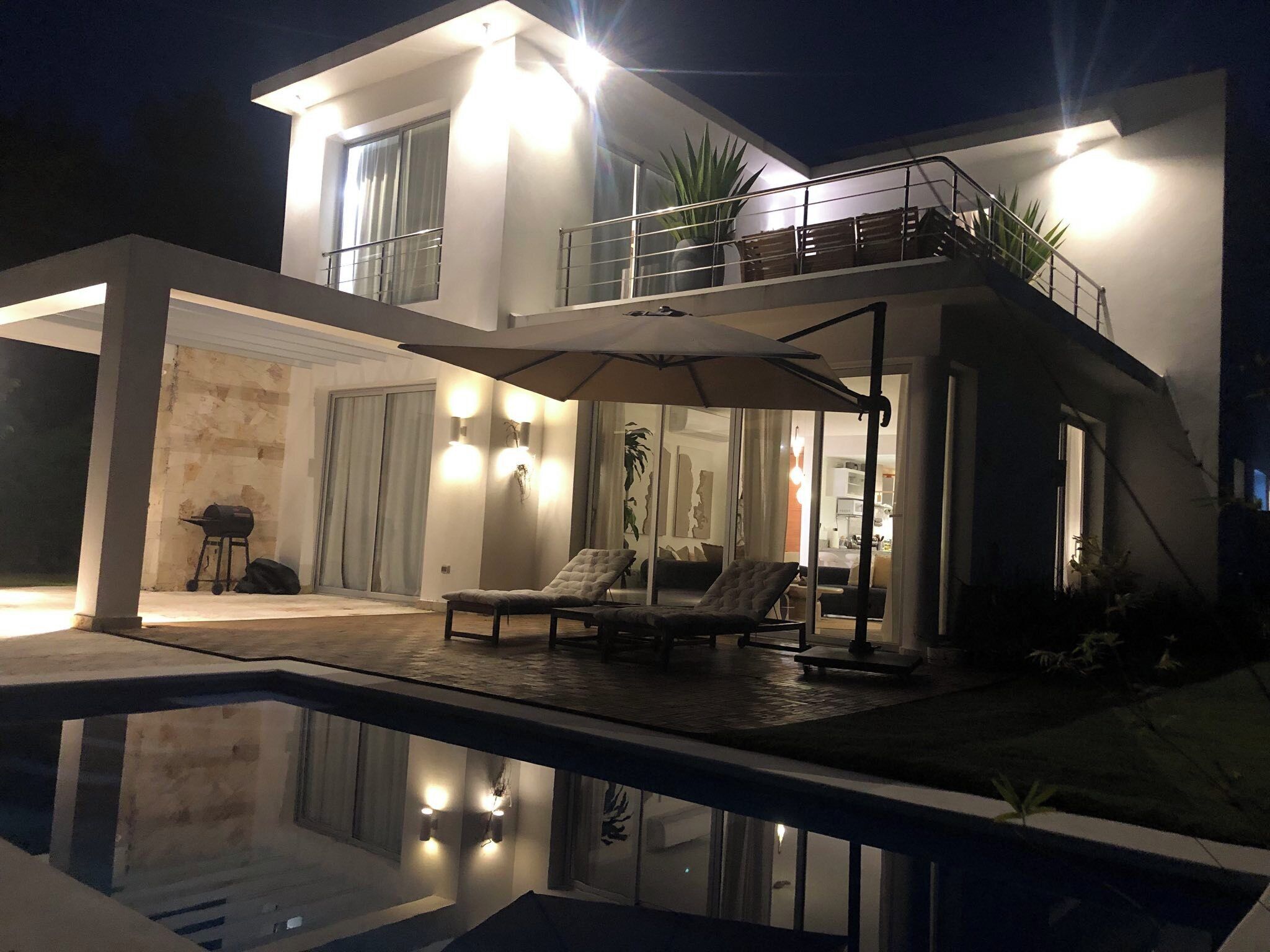 A modern two-story house with a swimming pool, outdoor seating, and a balcony.