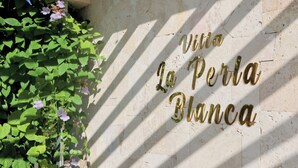 Een muur met de tekst 'Villa La Perla Blanca' en schaduwen van bladeren.