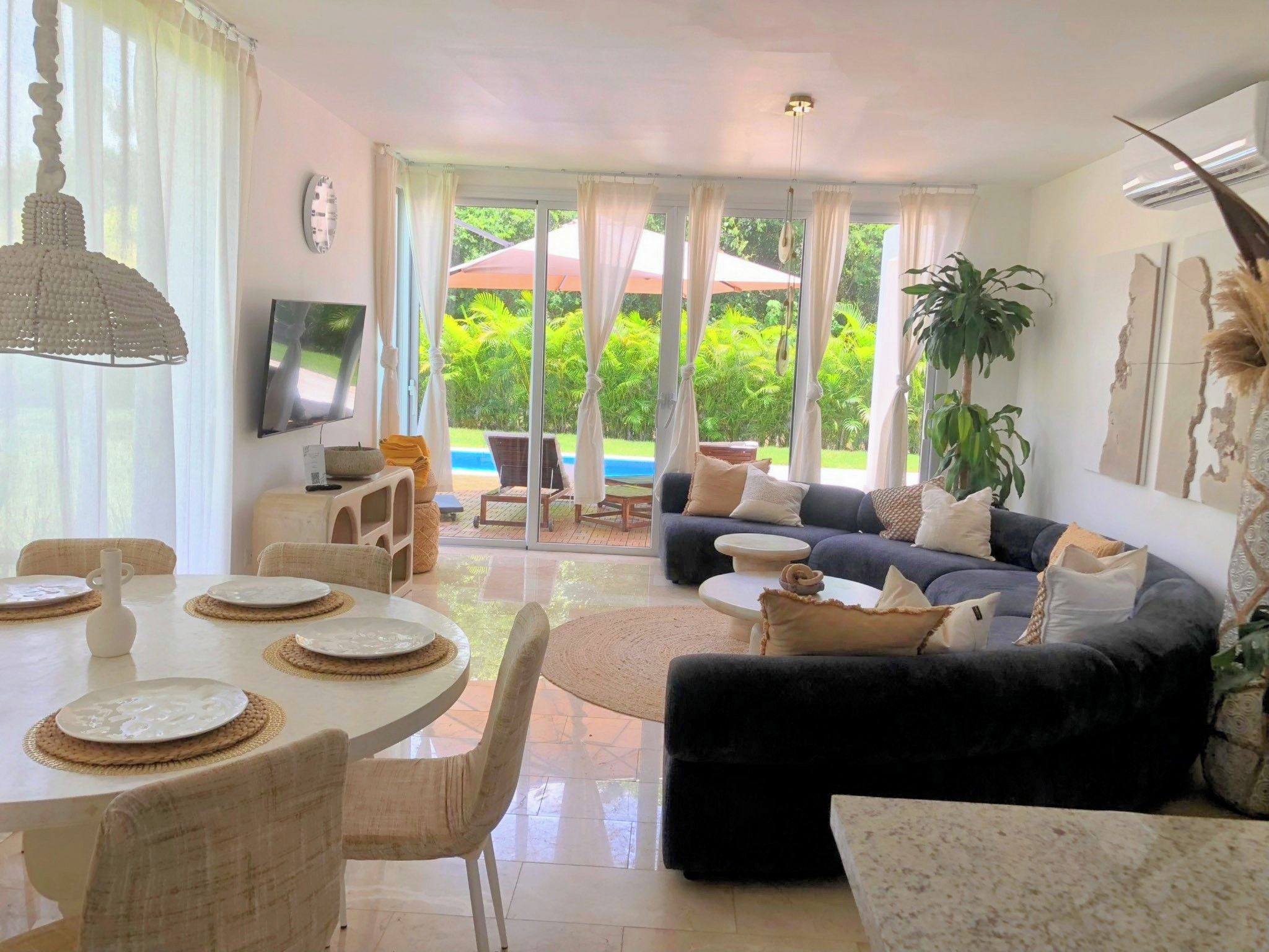 A living room with a sofa, a dining table set for four, and a TV mounted on the wall.