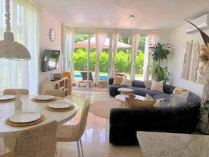 A living room with a sofa, a dining table set for four, and a TV mounted on the wall.