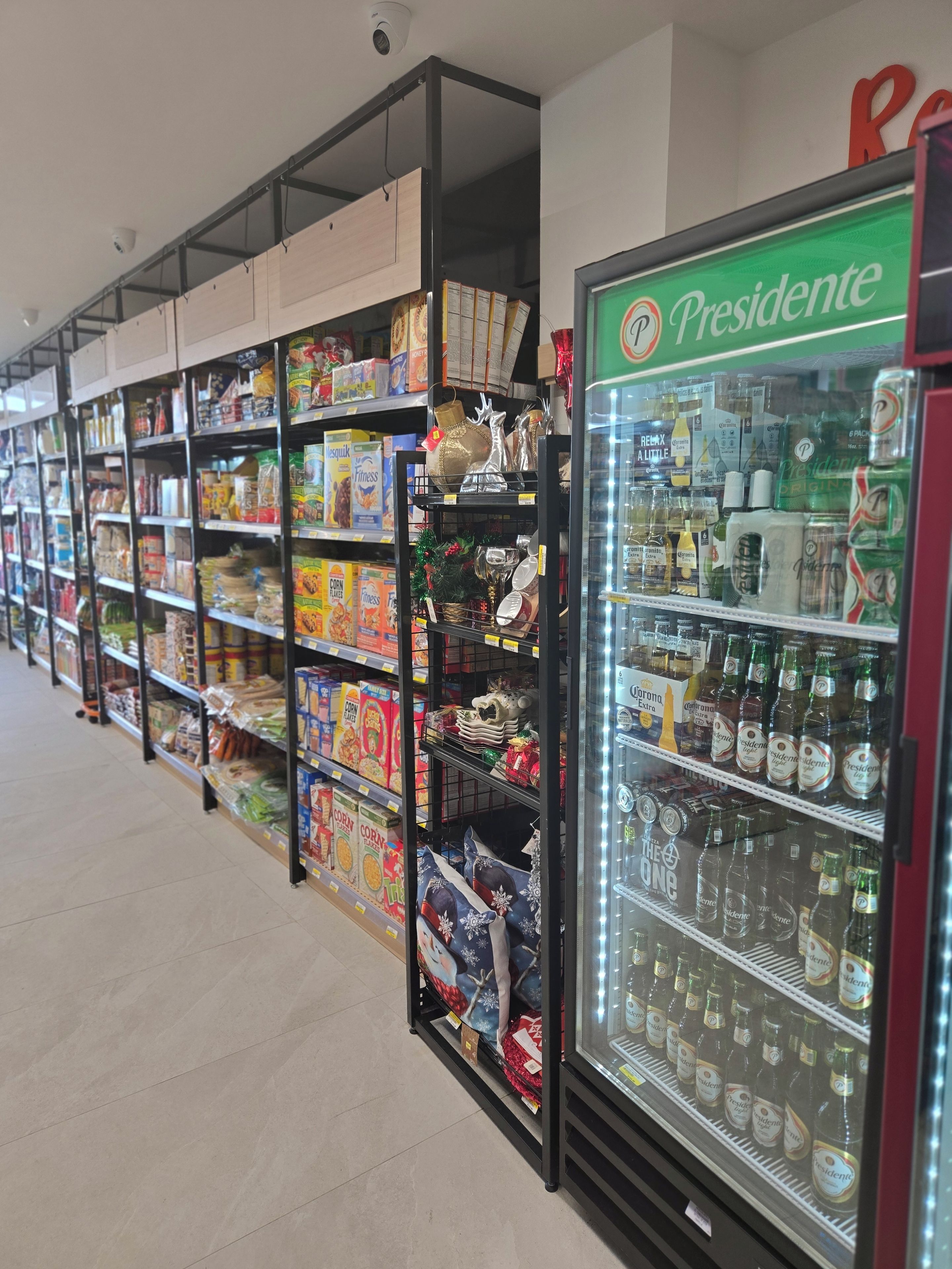 A grocery store aisle with shelves stocked with various food items and a refrigerated display case with beverages.