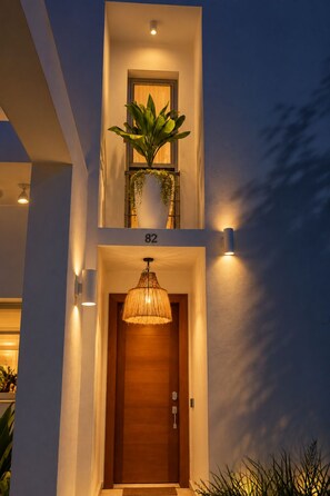 A modern building entrance with a wooden door, a potted plant, and a hanging light fixture.