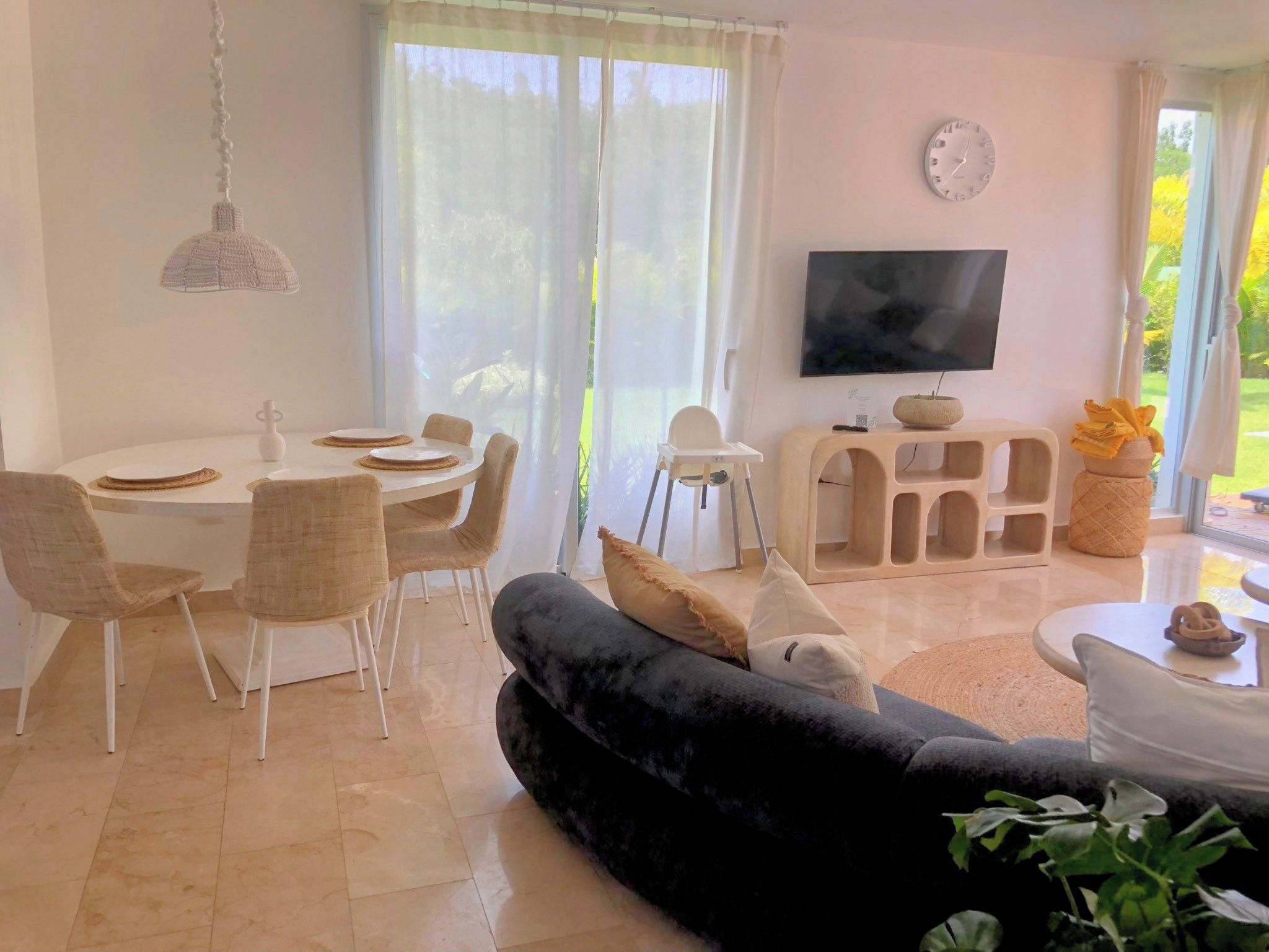 Un saló modern amb zona de menjador, un sofà negre, televisió i una finestra gran amb cortines.