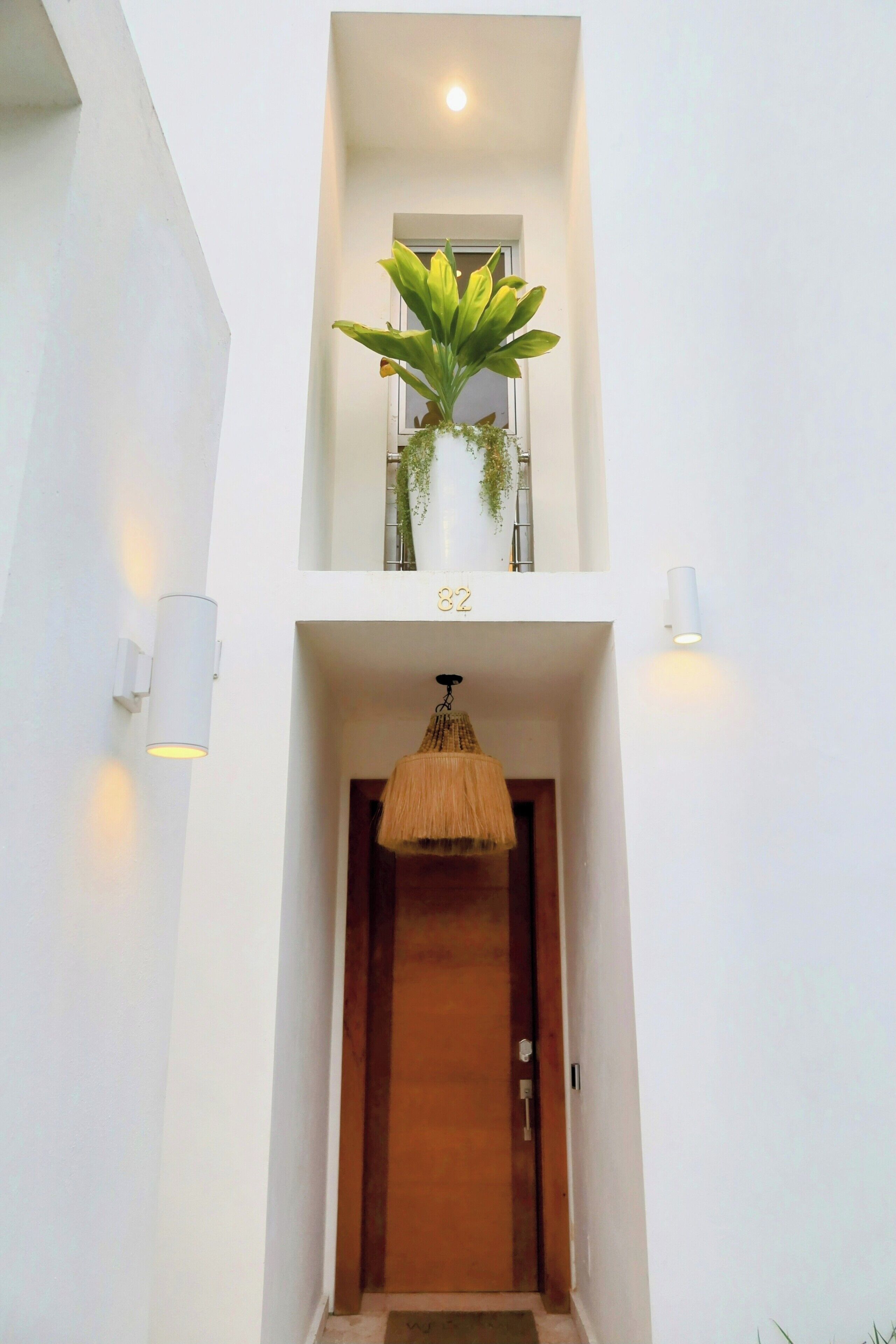 Une entrée moderne avec une porte en bois, un luminaire suspendu et une plante en pot sur un balcon.