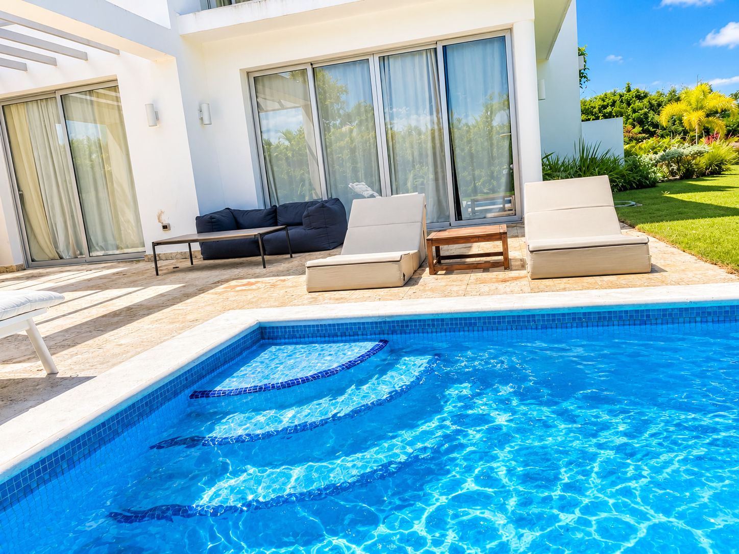 A swimming pool with lounge chairs and a sofa, surrounded by a white building with large windows.