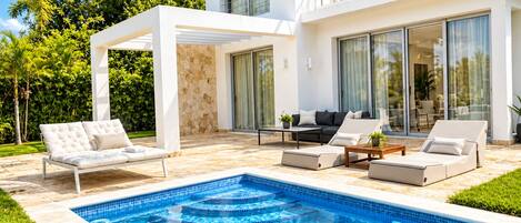 Un área de piscina moderna al aire libre con una piscina blanca, sillas de descanso y un patio con pared de piedra.