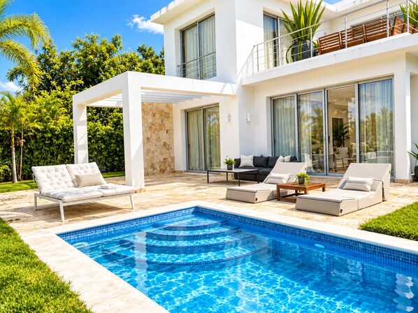 A modern outdoor pool area with a white pool, lounge chairs, and a patio with a stone wall.