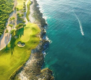 An aerial view of a coastal golf course with a clear path, a water body, and a visible golf cart track.
