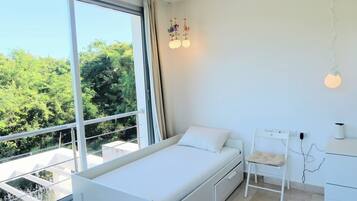 A bedroom with a bed, a desk, and a chair. There is a large window with a view of trees.