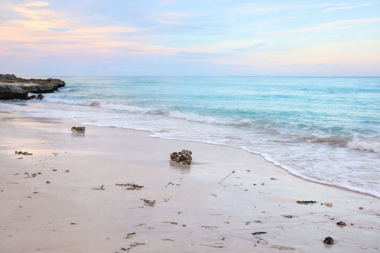 Une plage aux eaux calmes, un promontoire rocheux et des débris éparpillés.