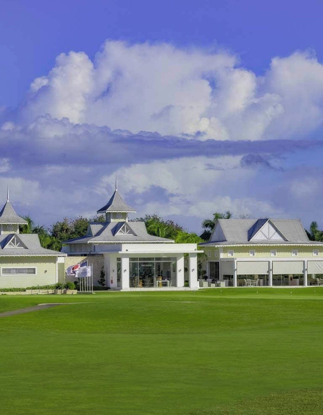 A golf course with a clubhouse featuring multiple buildings with distinct architectural styles, including a central pavilion with a glass facade.