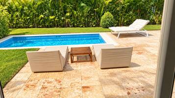A swimming pool with two lounge chairs and a wooden table.