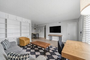 Ein stilvolles Wohnzimmer mit Sofa, Sessel, Couchtisch und Essbereich mit Fernseher und Tisch.