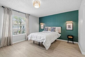 A bedroom with a bed, a window with curtains, a wall-mounted light fixture, and framed artwork. - Modern 3BR/2BA Apartment in the Heart of Houston (Houston)