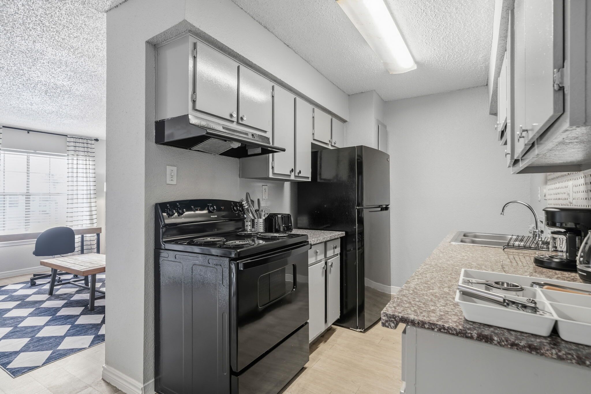 A modern kitchen with a gas stove, oven, stainless steel refrigerator, and granite countertop.