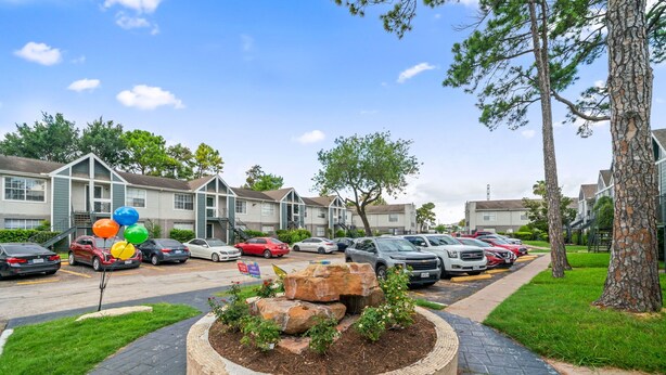 A residential area with apartment buildings, a parking lot, and a landscaped garden with rocks and plants.