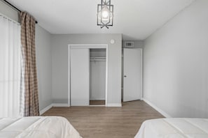 A room with two beds, a closet, a door, a light fixture, and a window with curtains. - Spacious 3 Bedroom Apartment: Perfect for Families (Houston)