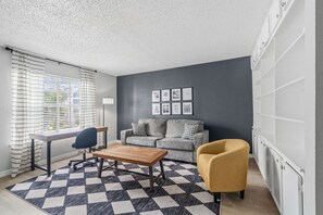 Bright living room with a charcoal accent wall, comfortable gray sofa, sunny mustard chair, and a dedicated desk beside the window. - Spacious 3 Bedroom Apartment: Perfect for Families (Houston)