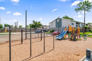 Ein Spielplatz mit Rutsche und Klettergerüsten, umzäunt und mit einem Gebäude im Hintergrund.