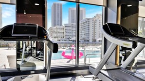 Ein Fitnessstudio mit Laufbändern und Blick auf eine Stadtlandschaft durch große Fenster.